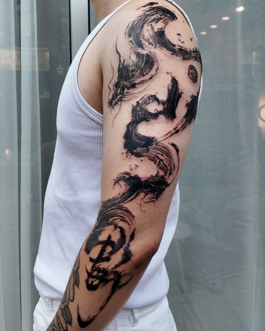 A person's arm displaying a large black ink wash style tattoo with flowing wave patterns.