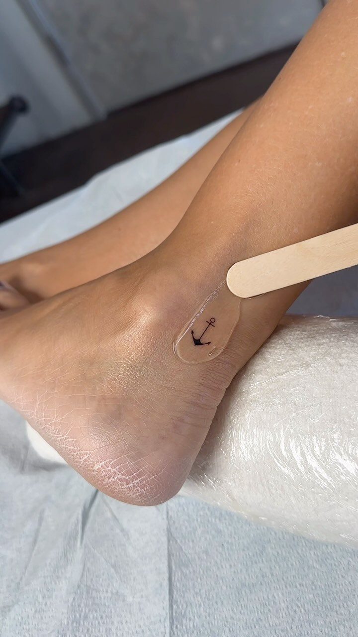 22 Delicate Tattoo Ideas for Light, Fine-Line Ink 18 A tiny black anchor tattoo on a person's ankle resting on a white surface.