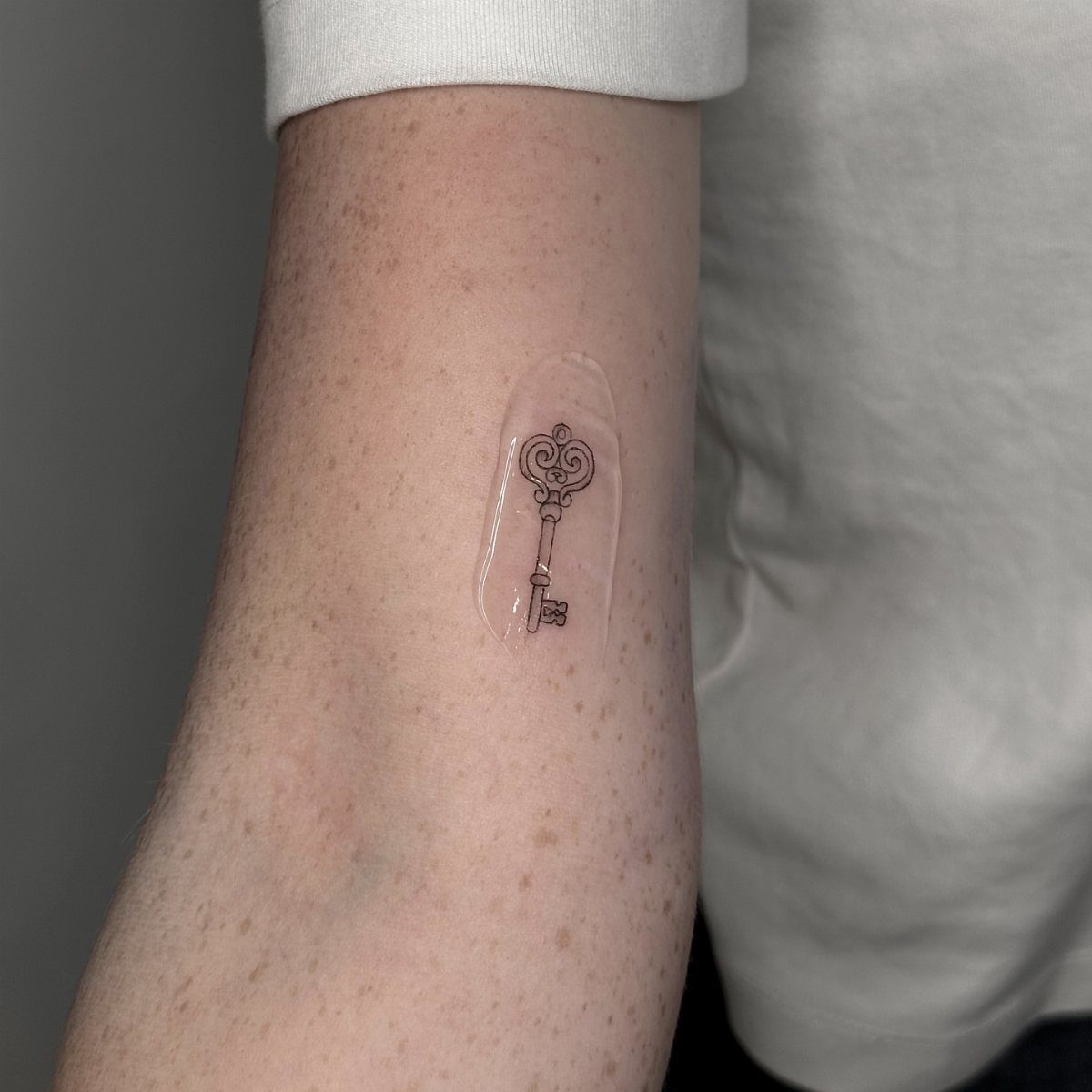 22 Delicate Tattoo Ideas for Light, Fine-Line Ink 17 A small vintage key tattoo inked in fine black lines on a freckled forearm.