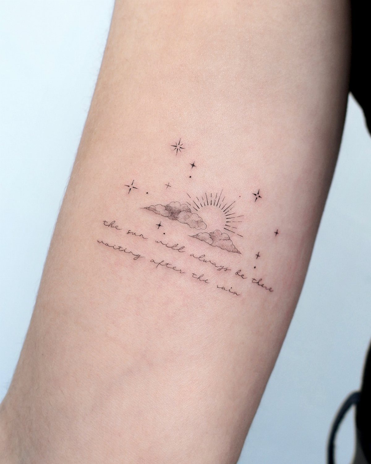 22 Delicate Tattoo Ideas for Light, Fine-Line Ink 9 A fine-line tattoo of a sun, clouds, stars, and cursive text on an arm.
