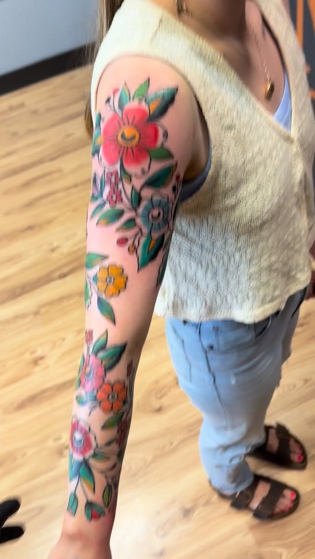A person's arm displaying a colorful American traditional floral tattoo with bold outlines.