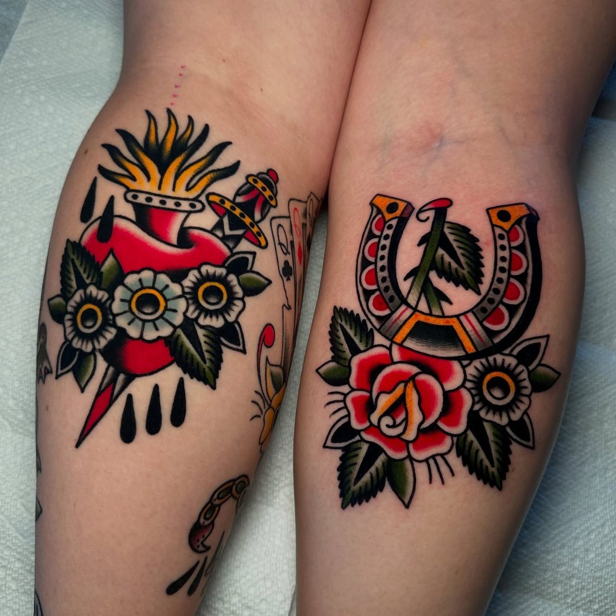 Two American traditional tattoos featuring a pierced heart and a horseshoe with roses on legs.