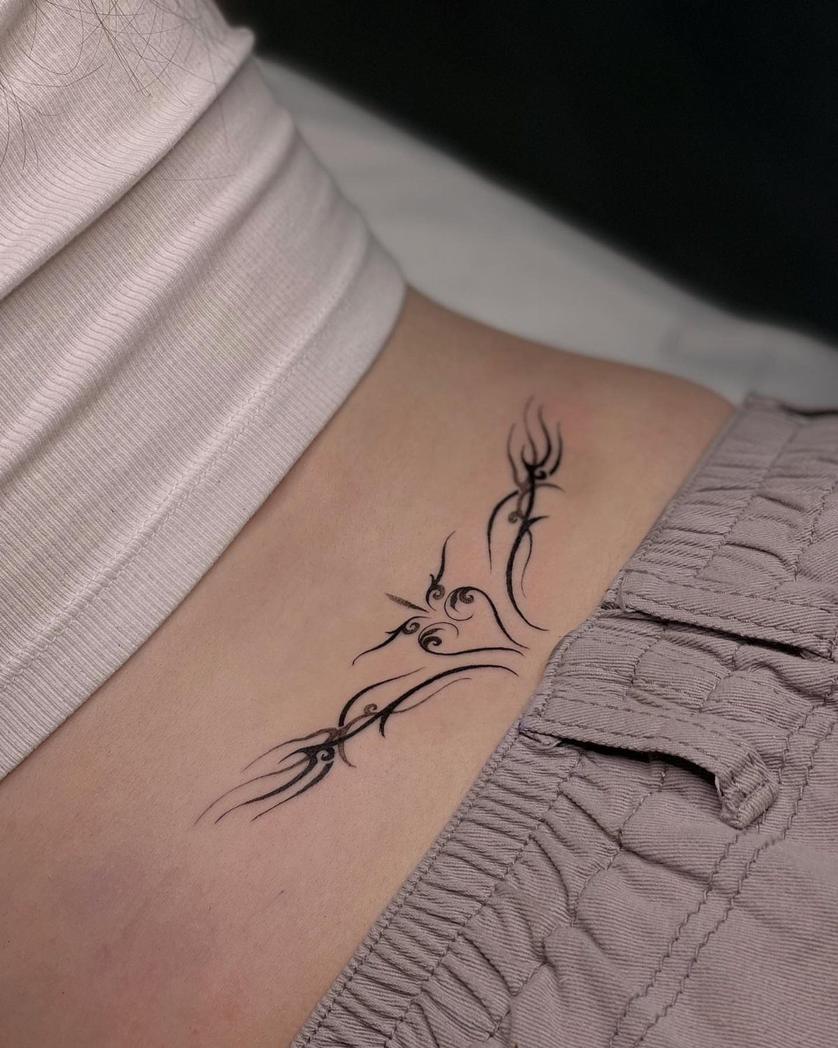 A black tribal style tattoo on a person's lower side back skin.
