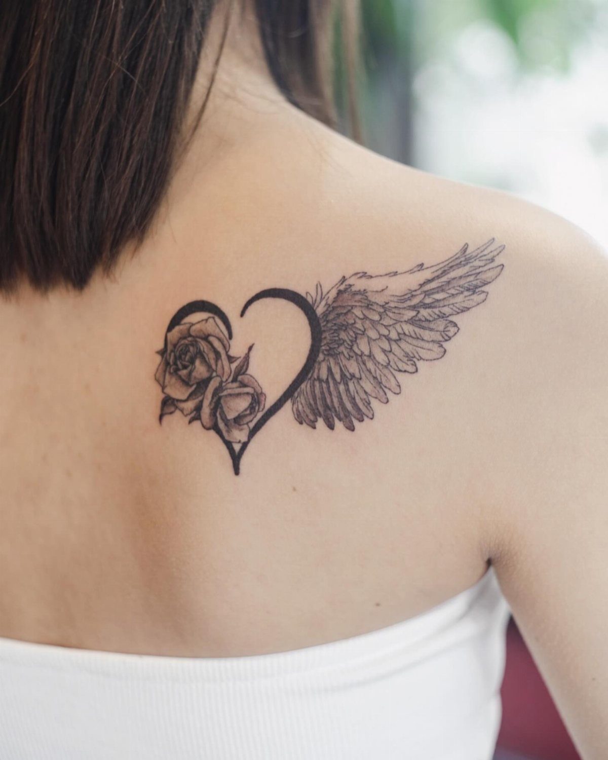 15 Tattoo Placement Heart Ideas for Meaning and Style 10 A black ink tattoo of a heart with a rose and a wing on a person's back.