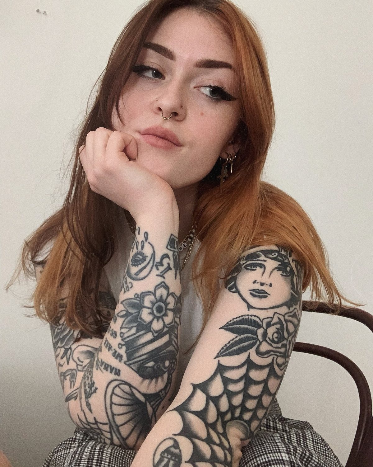 A young woman with reddish-brown hair displaying various black ink traditional tattoos on her arms.